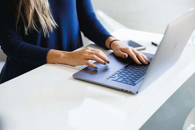Close-up of hands typing on a laptop on a clean white desk in soft natural light